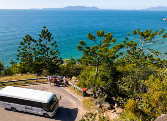 Drone shot of Bus parked at cliff top lookout. People looking out at the view